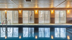 A pool with wooden walls and windows, a ladder, and a reflection of trees.