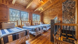 A log cabin with three beds, a stone fireplace, and large windows.
