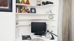 Un mueble blanco de entretenimiento con estantes que contienen libros, adornos, un reloj y un televisor.