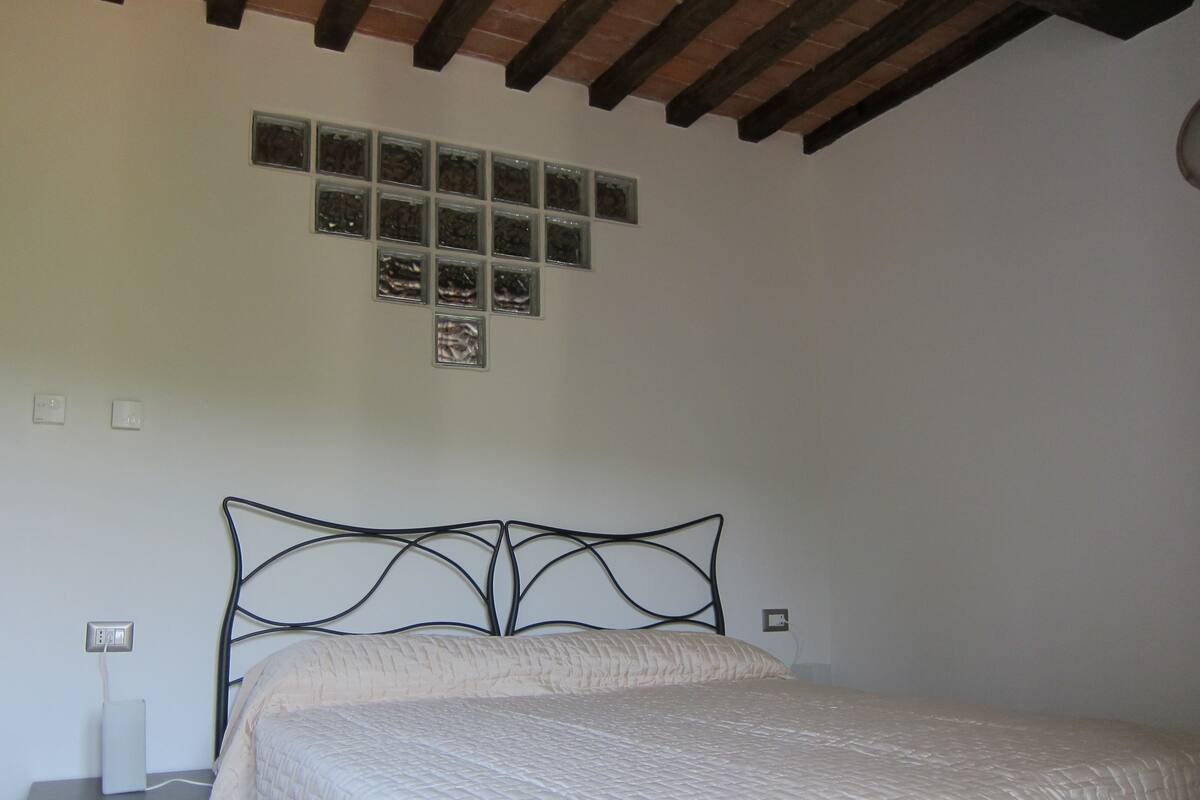 A bedroom with a bed, a nightstand, a power outlet, and a wall-mounted light switch.