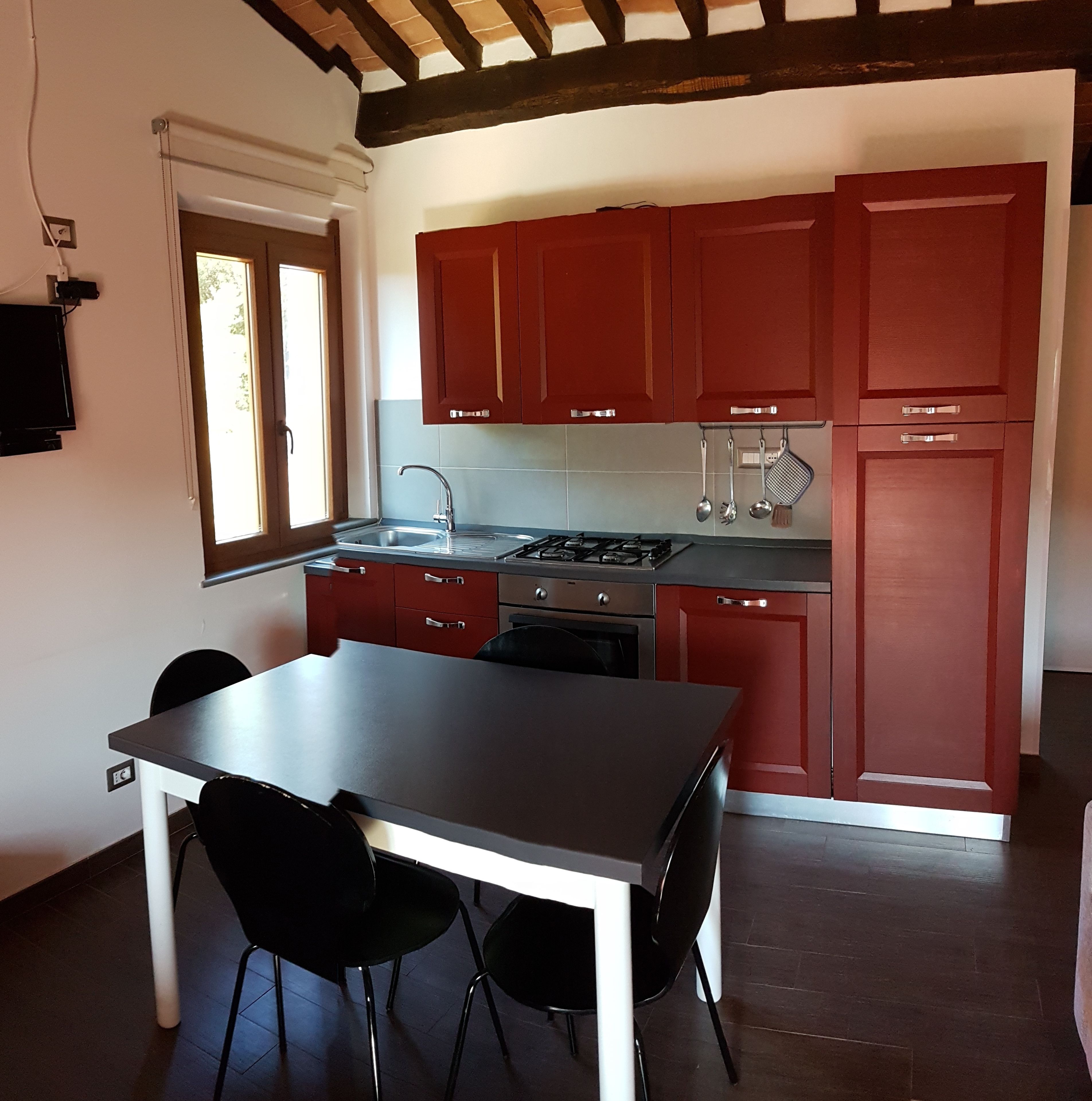 Une cuisine avec des placards rouges, une cuisinière à gaz, un évier et une table à manger avec des chaises.