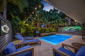 Un espace piscine agrémenté de chaises longues, de guirlandes lumineuses et d’un mur décoratif.