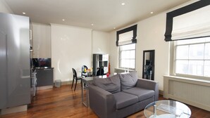Ein modernes Wohnzimmer mit einer grauen Couch, einem Glastisch und einem Essbereich mit Tisch und Stühlen.