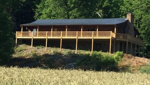 Una cabaña de madera con balcón, rodeada de árboles y un campo.