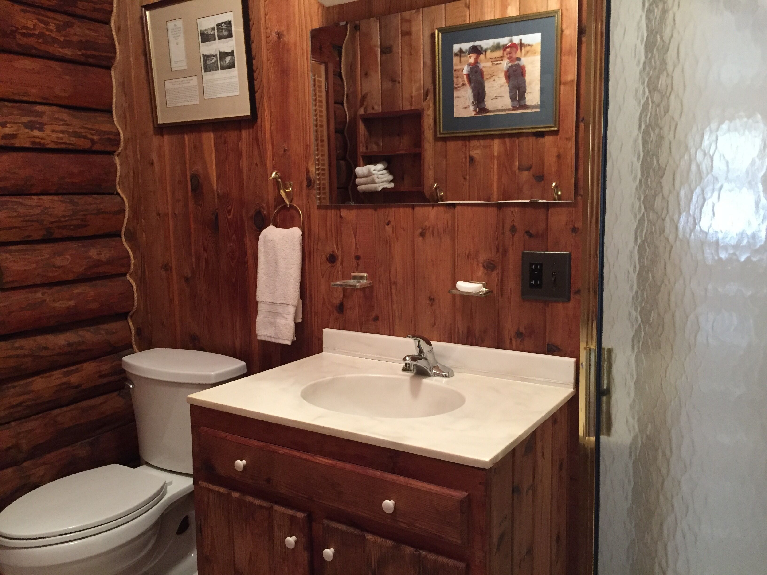 A wooden cabin bathroom with a toilet, sink, and wooden cabinets.
