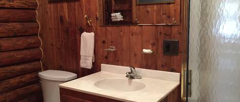 A wooden cabin bathroom with a toilet, sink, and wooden cabinets.