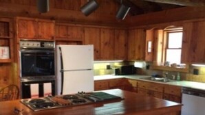 Una cocina tipo cabaña de madera con una isla central, horno empotrado, refrigerador y una ventana que proporciona luz natural.