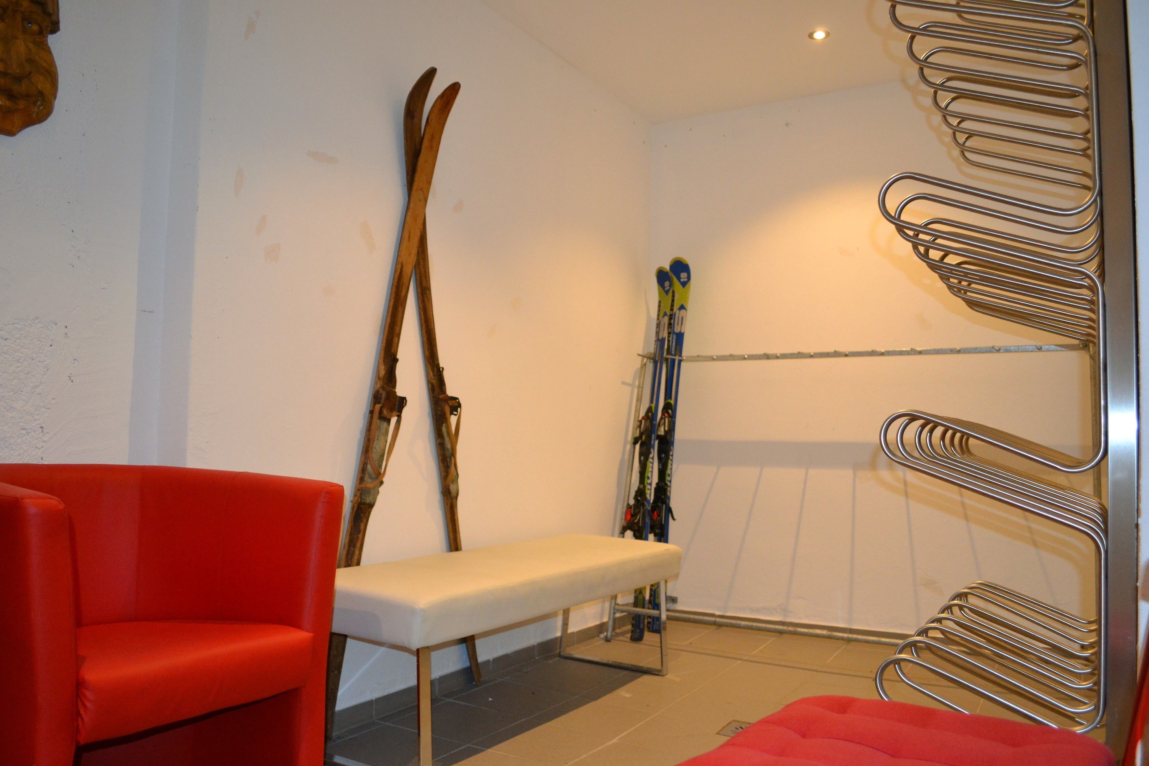 A ski room with a bench, red chair, and ski racks.