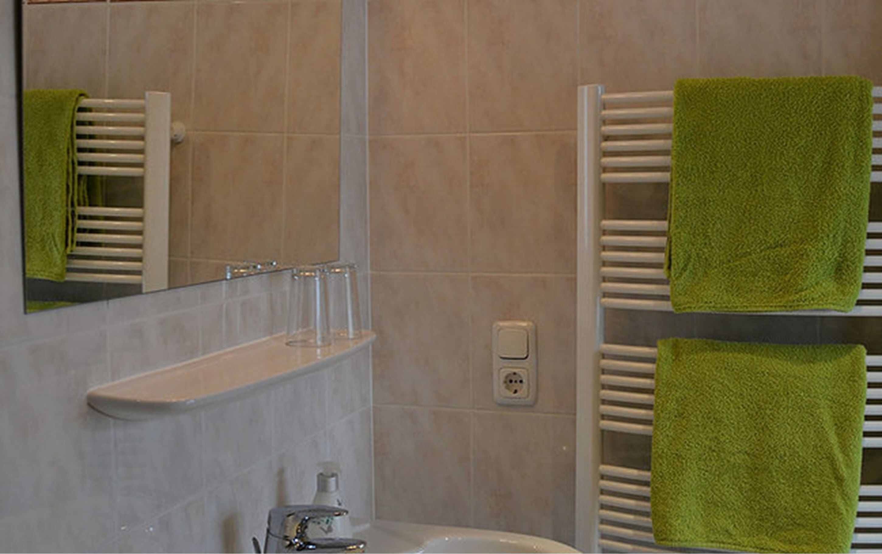 A bathroom with a sink, mirror, towel rack, and glassware.