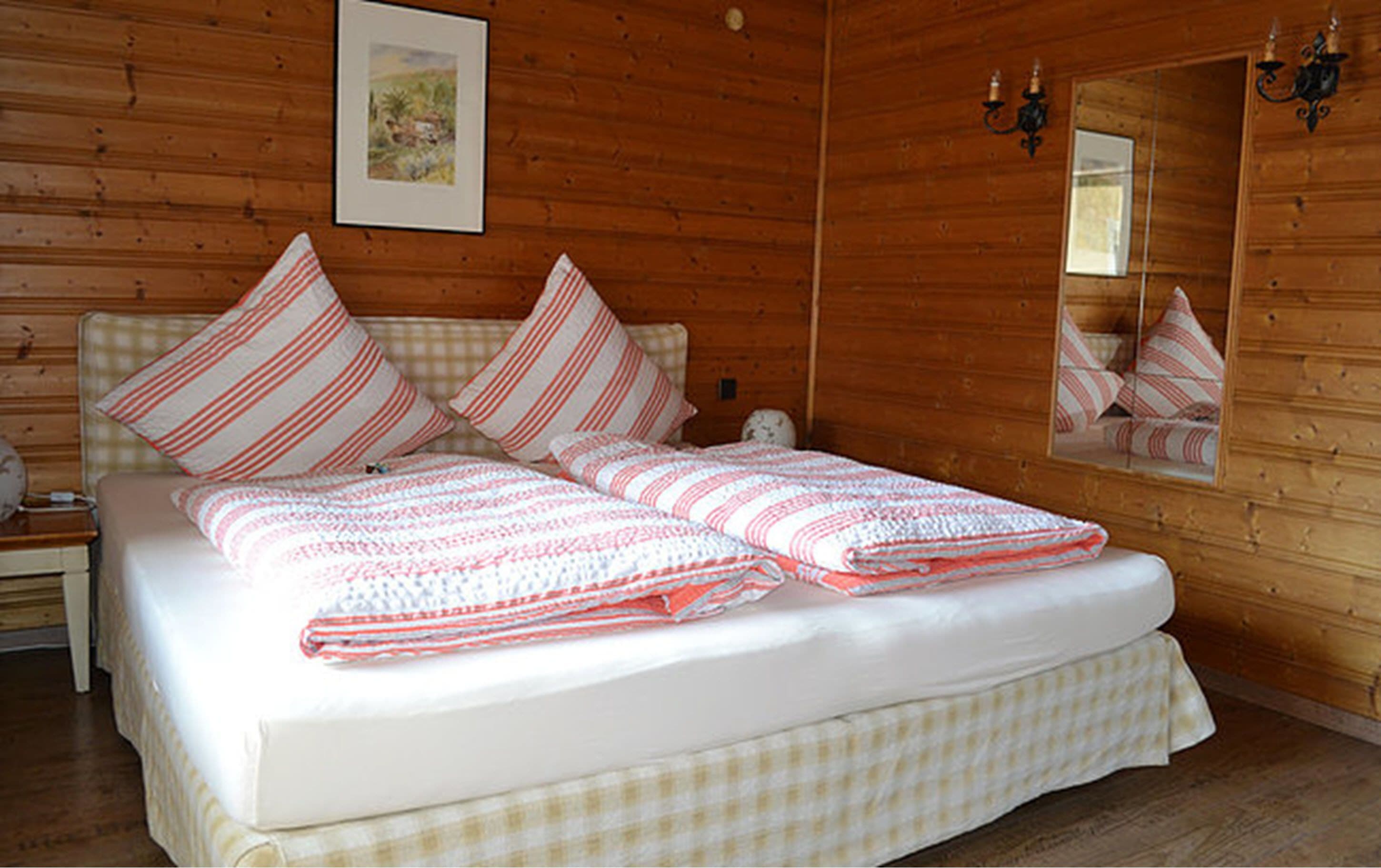 Ein Schlafzimmer in einer Holzhütte mit einem Bett, gestreifte Kissen, einer Steudecke, einem Nachttisch, einer Lampe und einem gerahmten Bild an der Wand.