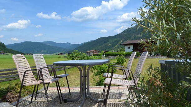 An outdoor seating area with a table and chairs, overlooking a mountainous landscape.