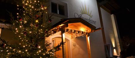 Een kerstboom met lichtjes en versieringen voor een gebouw met een bordje waarop 'Sunshine' staat.