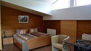 A bedroom with a loft-style bed, a chair, a small table, and a radiator.