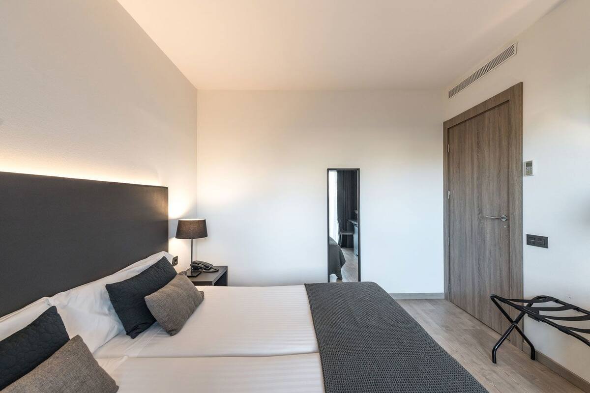 A modern hotel room with a large bed, bedside table, lamp, and a mirror.