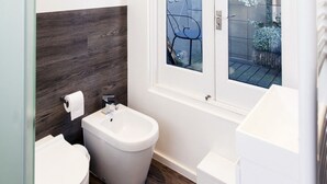 A modern bathroom with a bidet, toilet, and a window overlooking a balcony with plants.