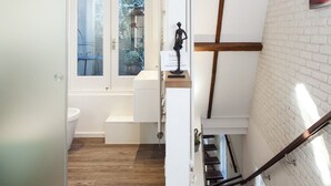 A modern interior with a staircase, a white wall with a brick pattern, and a window with a view of greenery.