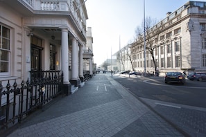 A street view with a sidewalk, buildings with classical architecture, and parked cars.