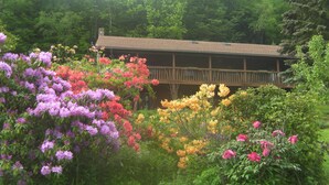 A wooden cabin with a balcony, surrounded by lush greenery and vibrant flowers. - Beautiful Getaway - Reynolds Farm Lodge  (Little Marsh)