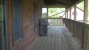 A covered wooden deck with a grill and a trash can. - Beautiful Getaway - Reynolds Farm Lodge  (Little Marsh)