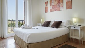 Una habitación de hotel con una cama grande, dos mesitas de noche, un velador, una ventana con cortinas y una obra de arte en la pared.