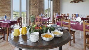 Un comedor con varias mesas dispuestas para el desayuno, con fruteros, vasos de jugo y productos para el desayuno.