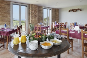 Un comedor con varias mesas dispuestas para el desayuno, con fruteros, vasos de jugo y productos para el desayuno.