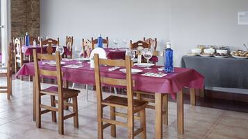 A dining area with tables set for a meal, wooden chairs, and a buffet table with food items.