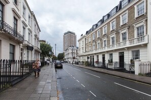 A street view of a residential area with a row of townhouses, a tall modern building in the background, and a sign for 'Bakers Hotel'. - Victoria Magical Atmosphere with Patios (London)