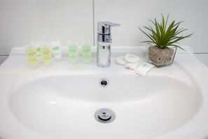A white bathroom sink with a chrome faucet, a small potted plant, and several Eden brand toiletries. - Victoria Magical Atmosphere with Patios (London)