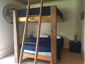 Un lit superposé avec une échelle en bois, une petite table avec une lanterne et un élément décoratif mural.