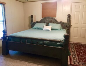 A bed with a wooden headboard, a green bedspread, and two pillows. - Beautiful Private River, Pool Table, Games, Lush Lawn, Pet OK, Kayak Heaven! (Leakey)