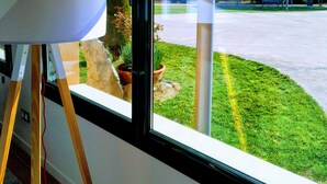 Ein Zimmer mit großem Fenster, Stehlampe und Blick auf einen Parkplatz und Grünflächen.