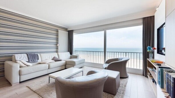 Una sala de estar moderna con un sofá, sillones, una mesa de centro y un gran ventanal con vista al mar.