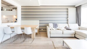 Una sala de estar moderna con un sofá blanco, un comedor con sillas blancas y una cocina con armarios blancos y un lavamanos.
