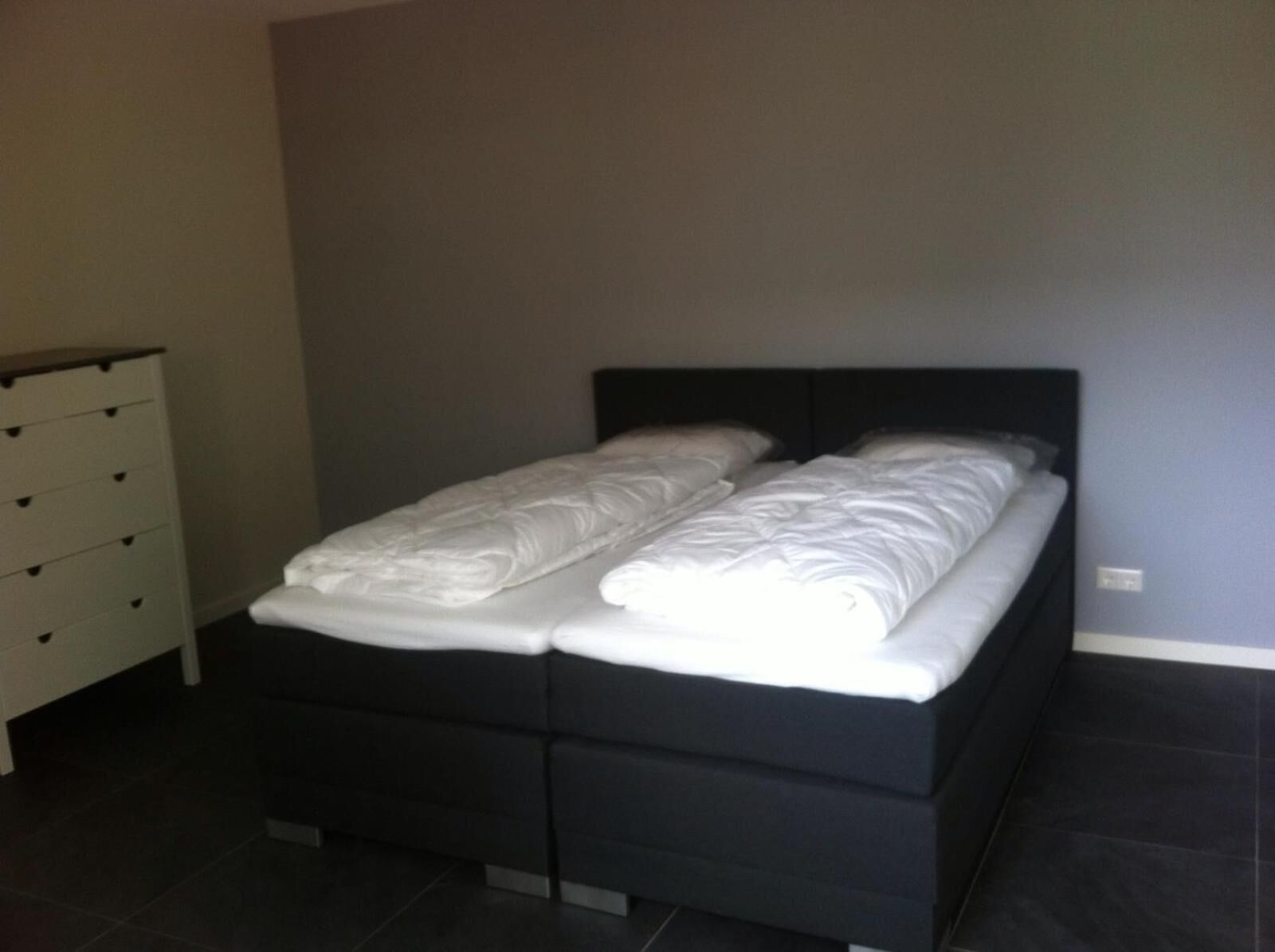 Une chambre à coucher avec un cadre de lit noir, du linge de lit blanc et une commode blanche dotée de nombreux tiroirs.