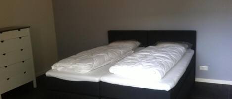 Une chambre à coucher avec un cadre de lit noir, du linge de lit blanc et une commode blanche dotée de nombreux tiroirs.