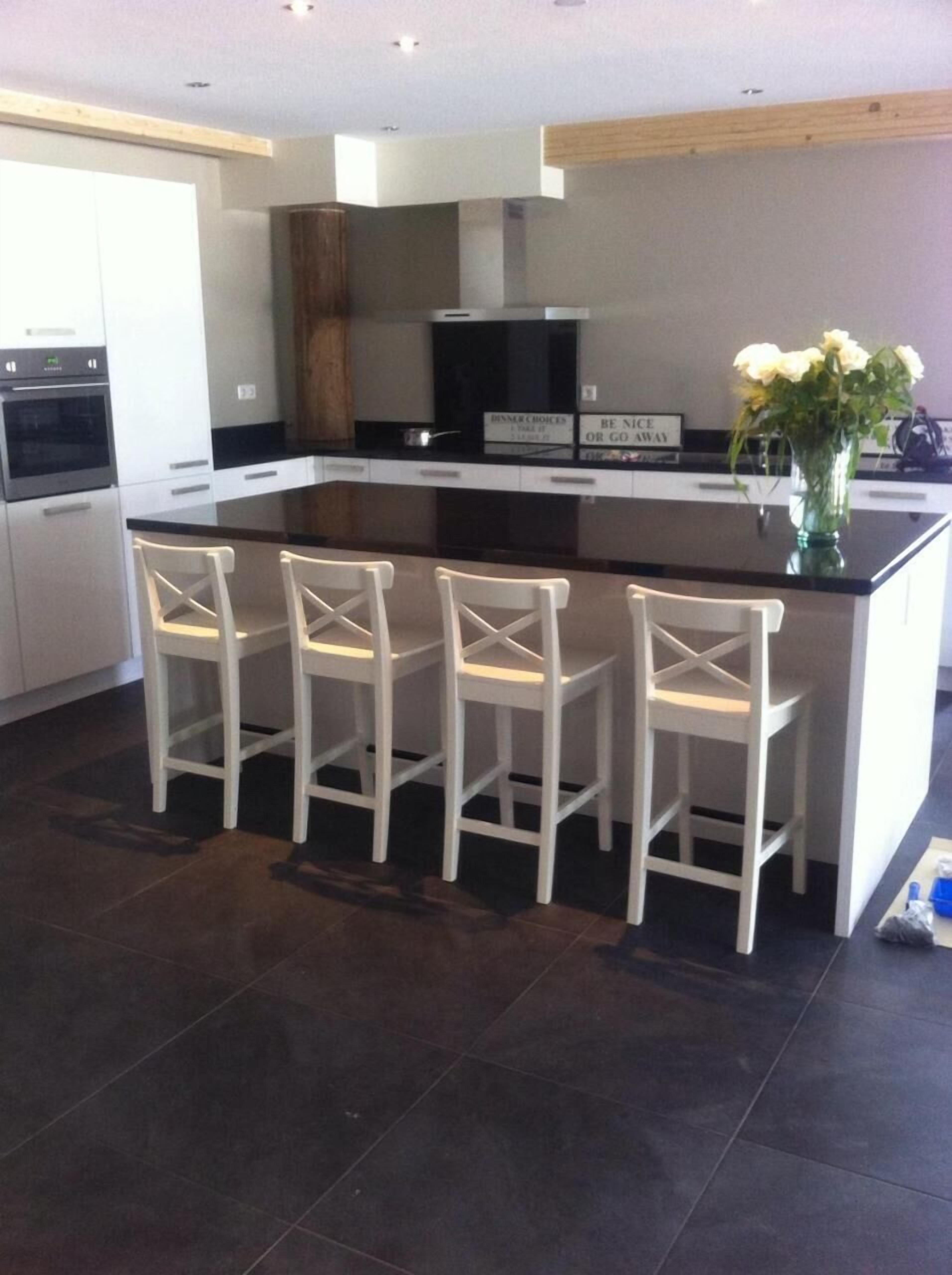 A modern kitchen with a central island, four white bar stools, and a vase of flowers.