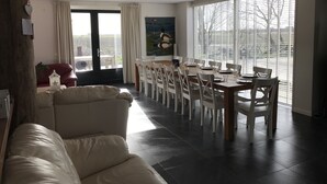 Een ruime woonkamer met een groot raam, een eethoek met een houten tafel en witte stoelen, en een rode bank.