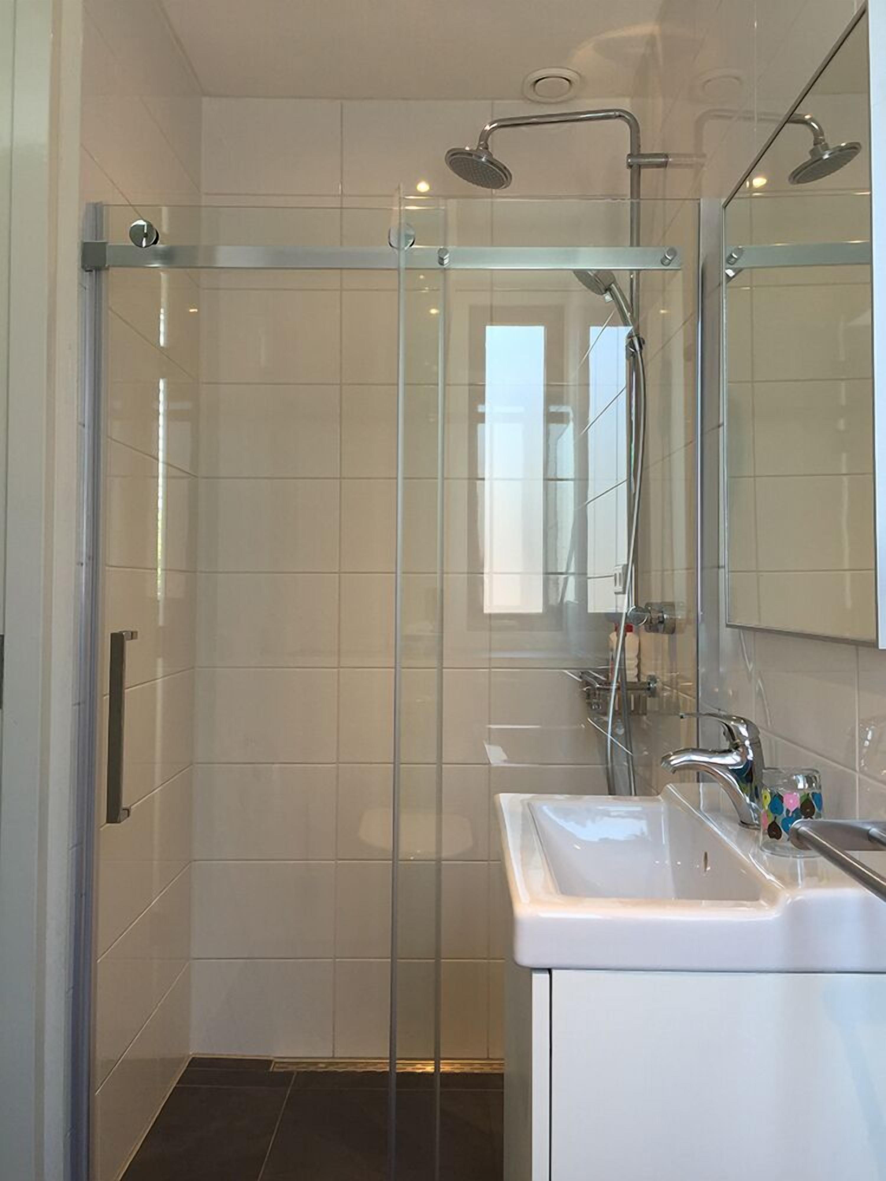 Une salle de bain moderne avec une douche à parois de verre, un lavabo blanc et un grand miroir.