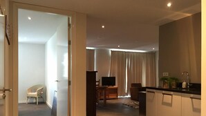 Een moderne woonkamer met een flatscreen televisie, een eethoek en een keuken met een zwart aanrecht en kastjes.