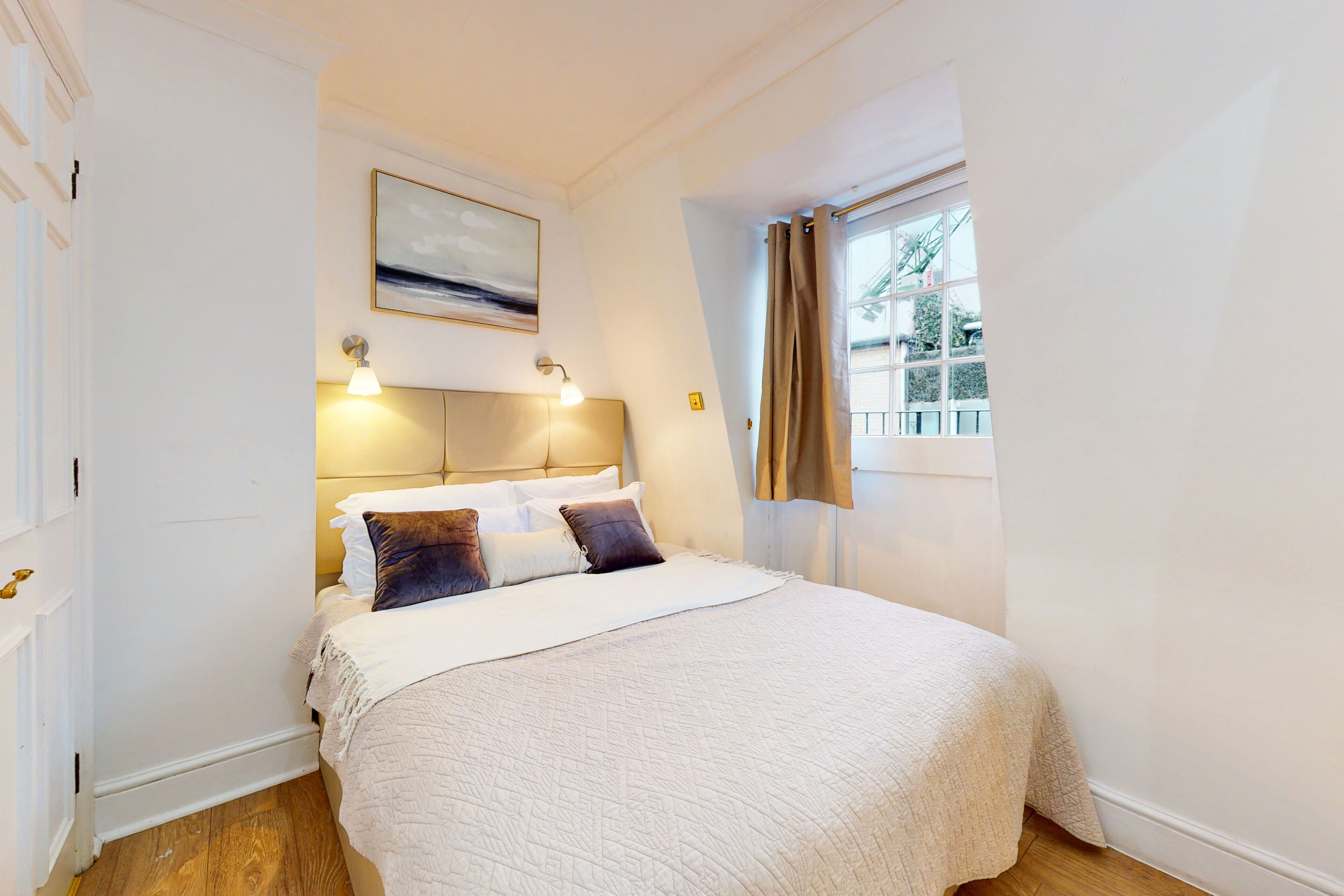 Een slaapkamer met een bed, twee bedlampen, een raam met gordijnen en een schilderij aan de muur.
