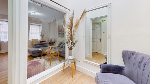 A modern living room with a glass coffee table, a sofa, and a large mirror reflecting the room. - Park Lane Apartments - Clarges St (London)