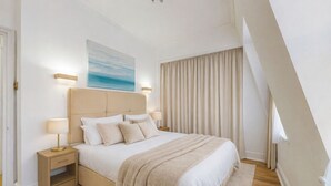 A bedroom with a large bed, two bedside tables, a headboard, a painting, and a window with curtains. - Park Lane Apartments - Clarges St (London)
