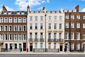 A row of terraced houses with uniform windows and balconies, a clear sky, and a sidewalk. - Park Lane Apartments - Clarges St (London)