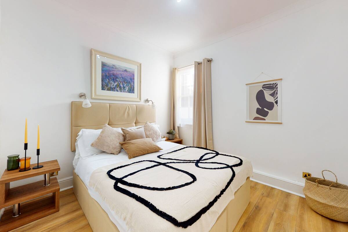 A bedroom with a bed, bedside table, lamp, and artwork on the wall.