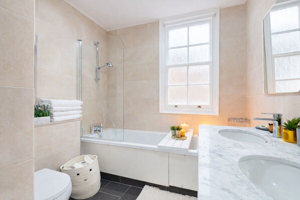 Un baño moderno con ducha de vidrio, bañera blanca, lavamanos grande y ventana sobre la bañera.