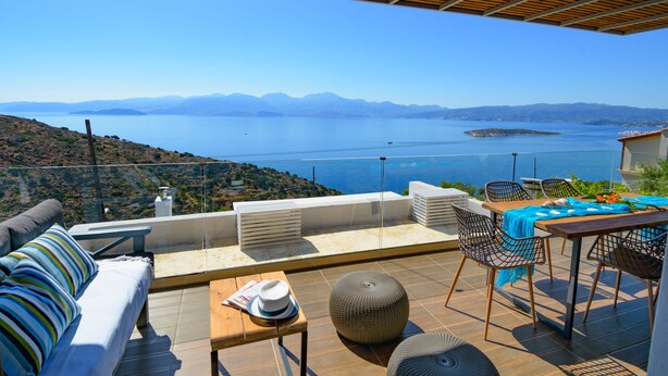 A terrace with a view of the sea, a sofa, chairs, and a table with a hat and newspaper. - Villa Olga (Agios Nikolaos)
