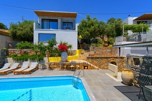 Un edificio moderno de dos plantas con piscina, zona de estar exterior y un muro de piedra.