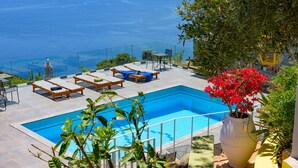 A pool area with lounge chairs and a view of the sea. - Villa Olga (Agios Nikolaos)