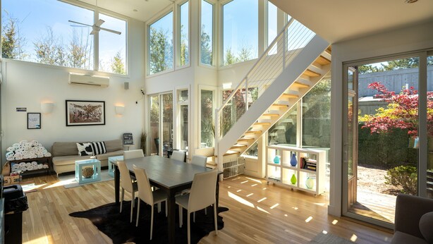 A spacious living area with a dining table, sofa, and a staircase leading to an outdoor deck.